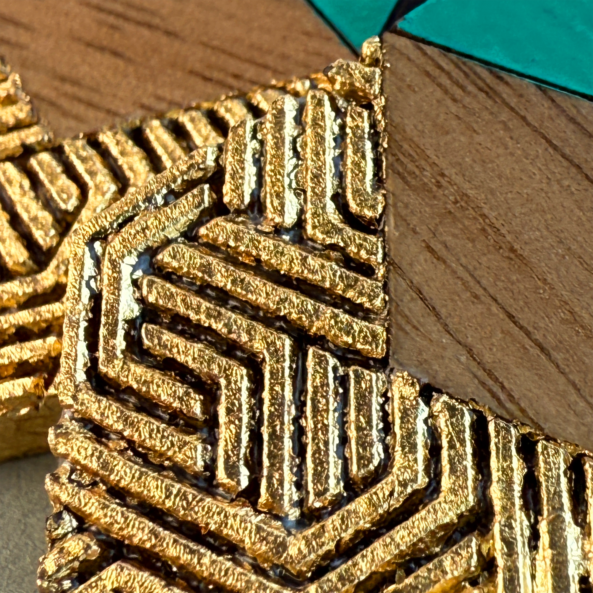 Close-up of detailed gold leaf pattern on geometric earrings, highlighting texture and artisan finish.