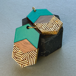 Teal and gold hexagon earrings styled in a stack on a black plinth for a premium display.