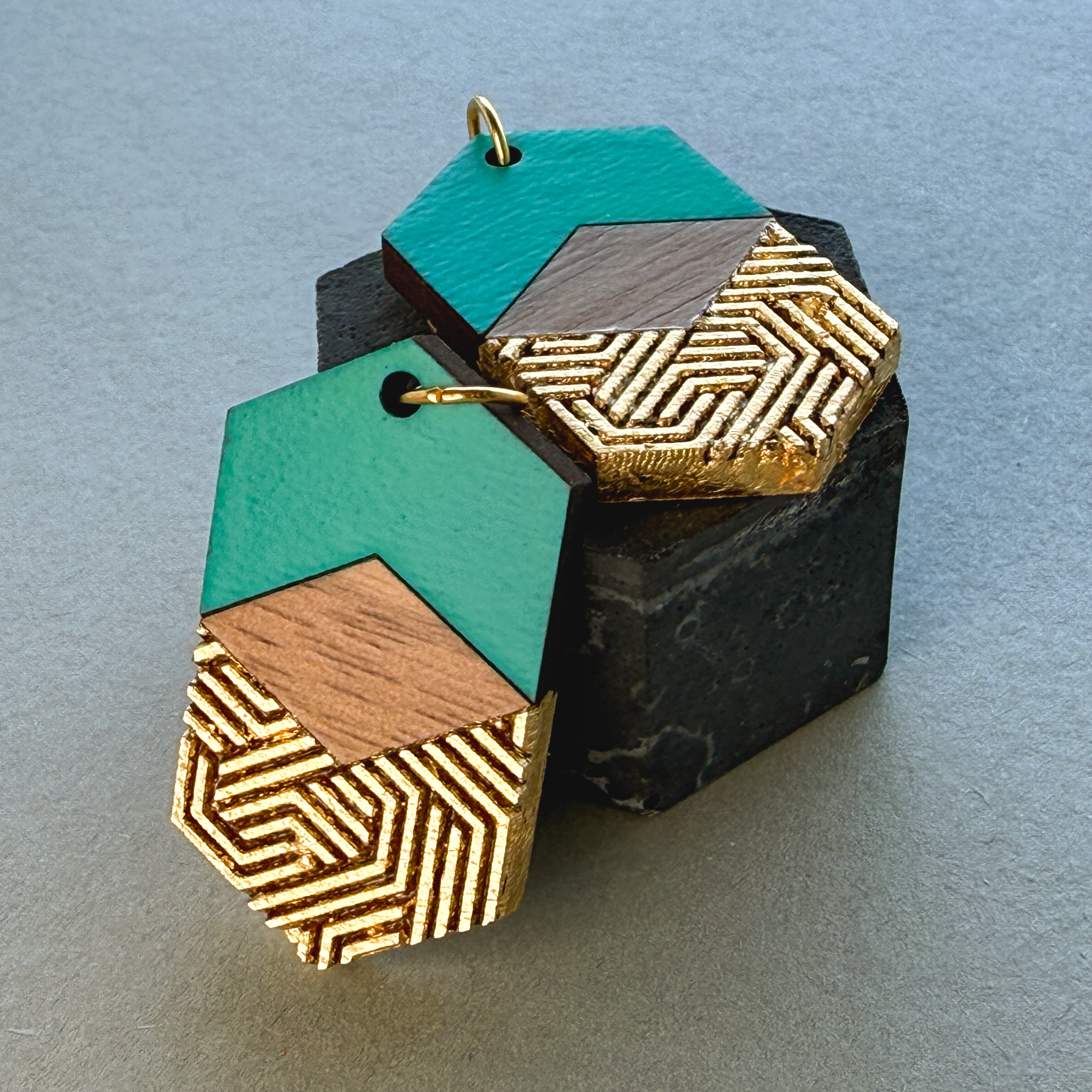 Teal and gold hexagon earrings styled in a stack on a black plinth for a premium display.